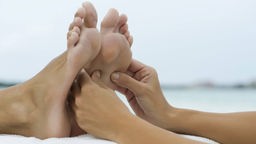 Das Bild zeigt Füße, die von zwei Händen massiert werden.
