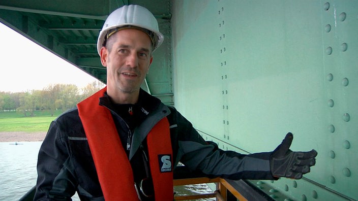 Techniker mit Helm vor den Nieten einer Rheinbrücke