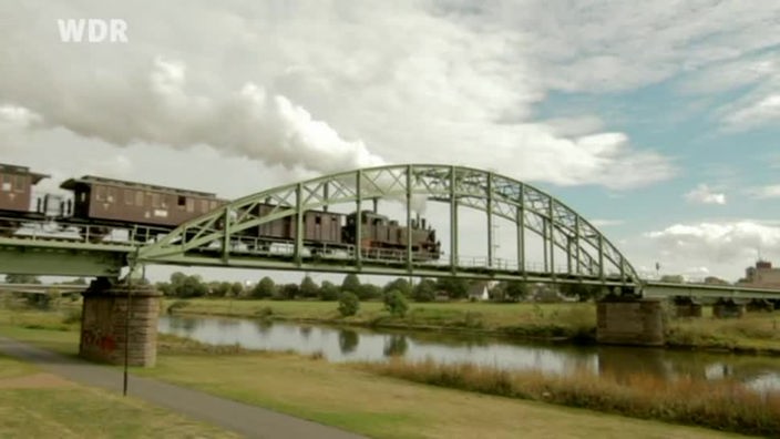 Alte Lokomotive fährt über eine Brücke.
