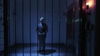 Ein Mann im Anzug in einem blau ausgeleuchteten Raum hinter einem Gitter