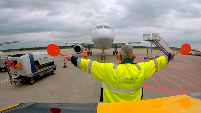 Fluglotse mit gelber Warnweste vor einem Flugzeug