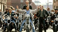 Horst Schimanski auf einer Harley, Kommissar Thanner stehend hinter ihm umgeben von jungen Männer in Lederkluft und Motorrädern. 