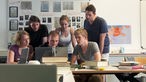 Junge Menschen in einem Seminarraum, sie schauen gemeinsam auf einen Computerbildschirm