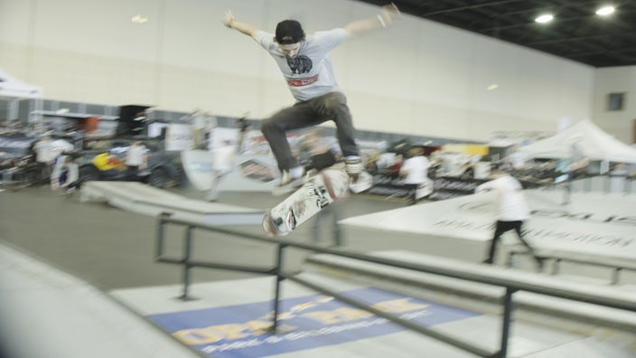 Ein Jugendlicher in einer Skaterhalle versucht einen Trick auf einem Geländer