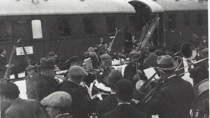 Historisches Schwarz-Weiß-Foto eines ankommenden Zuges mit Wintersportlern