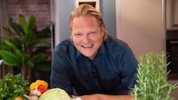 Björn Freitag in der Küche mit einem Korb Gemüse. 