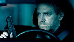 Wallander (Kenneth Branagh) sitzt mit einer Pistole im Auto