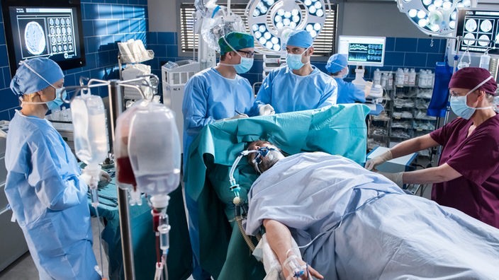 In einer Not-Operation, versuchen Elias Bähr (Stefan Ruppe, 2.v.l.) und Dr. Niklas Ahrend (Roy Peter Link, 2.v.r.) Geros Gehirn zu entlasten.