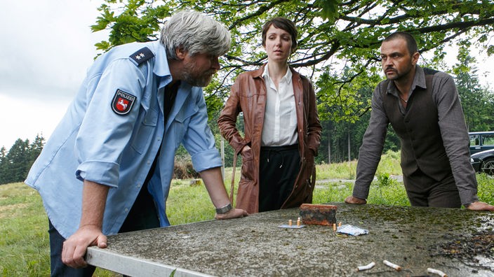 Koops (Aljoscha Stadelmann) erklärt Hagen (Michael Rotschopf) und Simone (Julia Koschitz) seinen Plan die Bank zu überfallen anhand von Zigaretten.