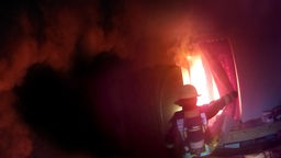 Ein Feuerwehrmann vor einem brennenden Wohnhaus 