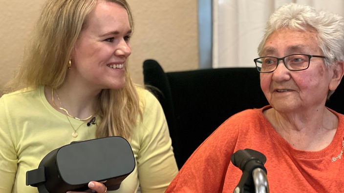 junge Frau zeigt einer älterin Seniorin, wie man eine VR Brille benutzt