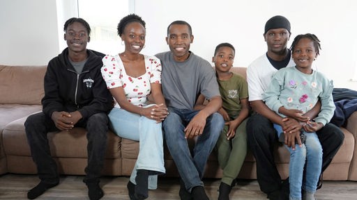 sechs köpfige Familie posiert auf Sofa und lächelt in die Kamera