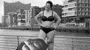 Frau im Bikini steht an Promenade, die Elbphilharmonie Hamburg im Hintergrund und lächelt selbstbewusst in die Kamera