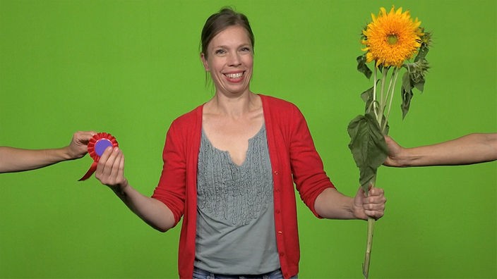 Frau steht vor einem grünen Hintergrund. es werden jeweils eine Medaille und eine Sonnenblume von links und rechts eingereicht