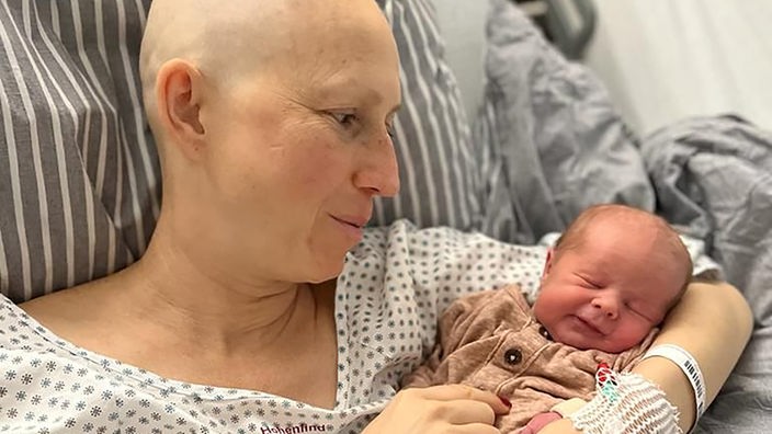 Krebskranke Frau hält stolz ihr neugeborenes Kind in den Arm. 