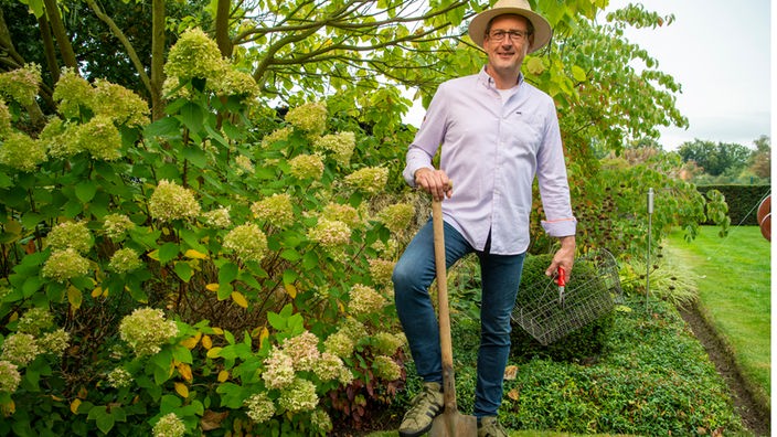 Stefan Greven mit Gartenwerkzeug vor Hortensien