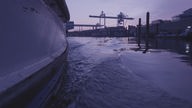 Ein Schiff durchfährt einen Kanal im Duisburger Hafen und verursacht eine Bugwelle.