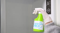 Das Bild zeigt eine Sprühflasche mit Reinigungsmittel vor einem Kühlschrank.