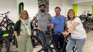 Das Bild zeigt Yvonne Willicks und Daniel Aßmann mit Familie ten Brink in einem Fahrradladen mit E-Bikes.