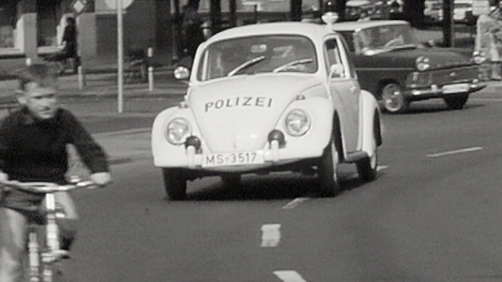 sw-Foto, ein Polizei-VW-Käfer fährt in eine Kurve, im Vordergrund ein Junge auf einem Fahrrad