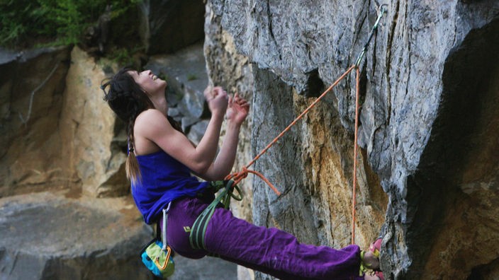 Junge Frau klettern am Seil gesicheet einen Felsen empor