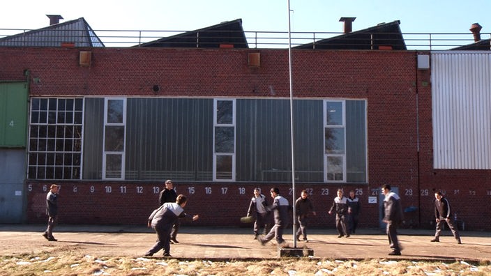 Jugendliche spielen auf einer Fläche zwischen Werkshallen Fußball