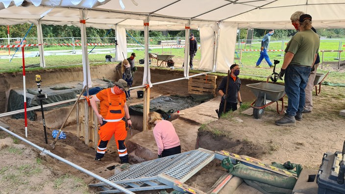 Menschen arbeiten an einer Ausgrabungsstelle, die mit einem Zeltdach geschützt ist