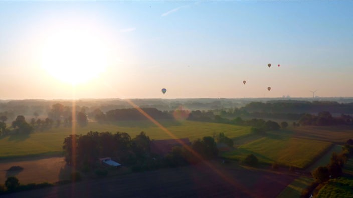 Totale Lauftaufnahme: Heißluftballons über einer Wisenlandschaft.