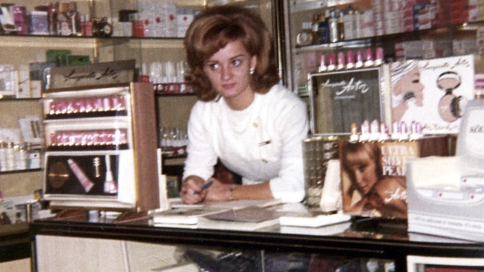Ein junge Frau in weißem Kittel lehnt an einem Verkaufstresen