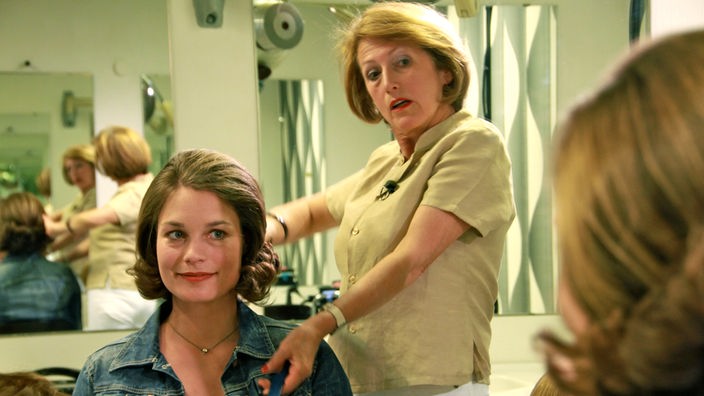 Eine junge Frau im Frisörsalon schaut sich mit der Friseurin im Spiegel die neue Frisur an.