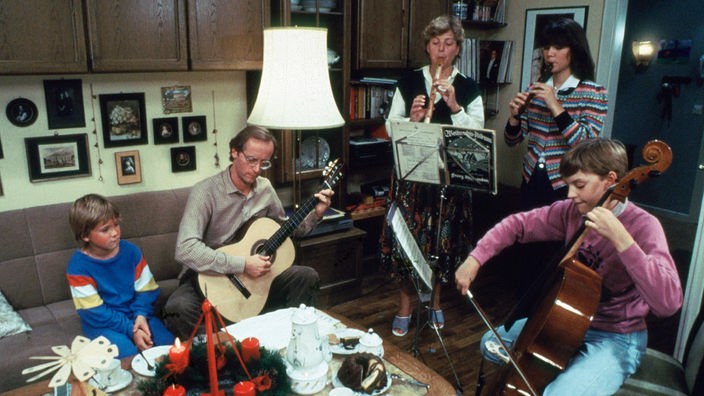 Eine Familie im Wohnzimmer bei Hausmusik, auf dem Tisch ein Adventskranz