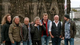 Gruppenfoto der Band, im Hintergrund der Kölner Dom
