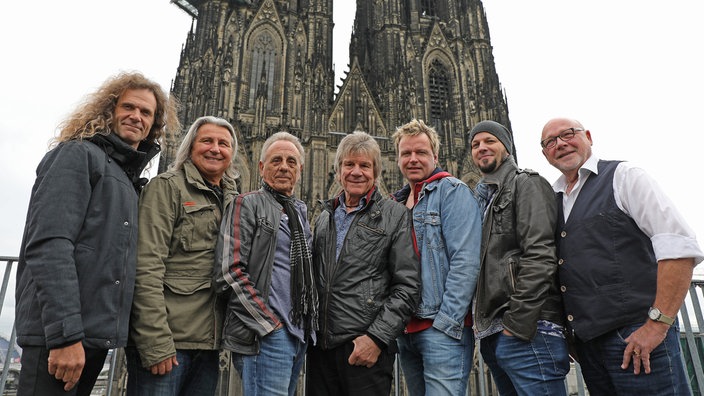 Gruppenfoto der Band, im Hintergrund der Kölner Dom