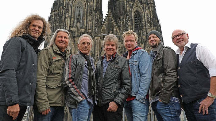 Gruppenfoto der Band, im Hintergrund der Kölner Dom