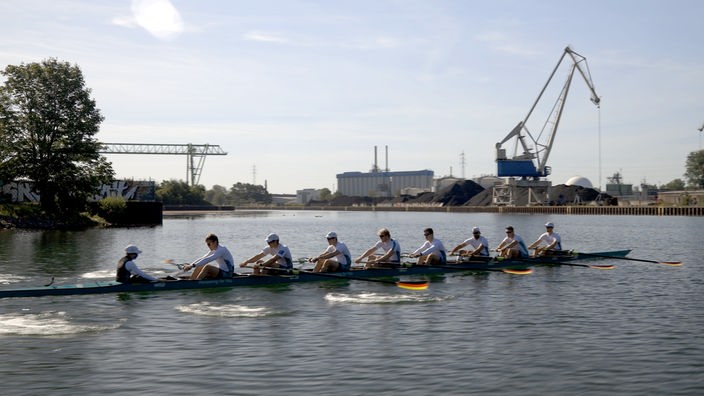 Ein Sport-Ruderboot im Kanal, im Hintergrund eine Industriekulisse mit einem großen Kran
