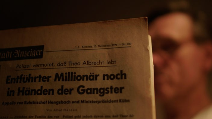 Spielszene Mann liest Zeitung, Schlagzeile Millionär noch in den Händen der Gangster