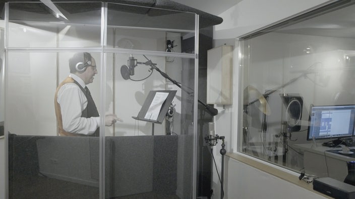 Ein Mann steht in einer Glaskabine am Mikrofon
