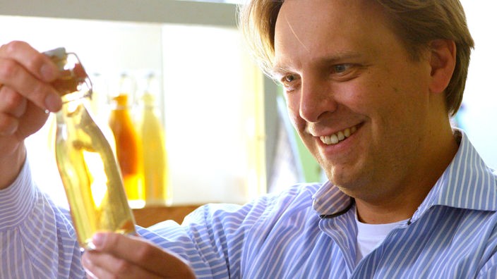 Ein Mann steht in einem Labor und schaut lächelnd auf eine Flasche