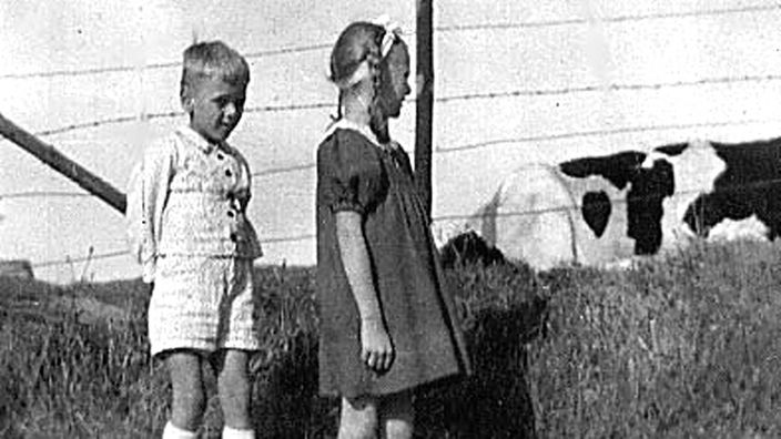 sw-Foto: Ein Junge und ein Mädchen stehen an einem Zaun, im Hintergrund sind Kühe