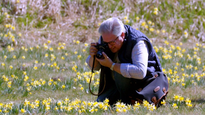 Ein Mann fotografiert hockend auf einer Narzissenwiese