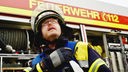 Ein Feuerwehr-Mann in voller Ausrüstung steht vor einem Feuerwehrwagen