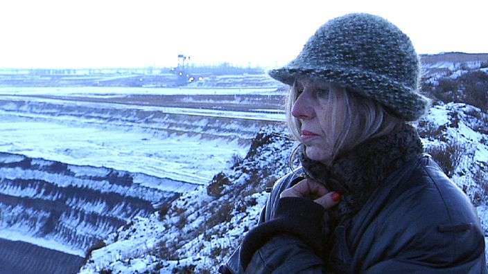 Eine Frau blickt traurig in eine verschneite Tagebaulandschaft