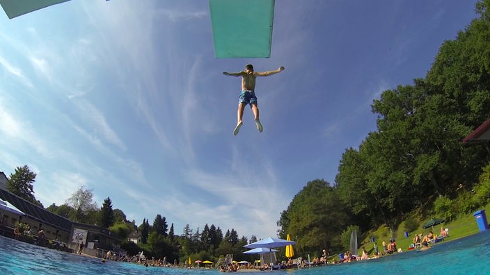 Ein Junge springt vom Sprungturm in ein Schwimmbecken