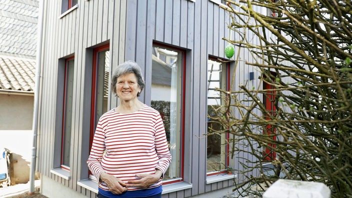 Eine ältere Dame steht glücklich vor ihrem Mini Haus.