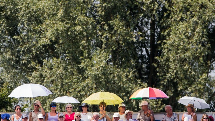Zuschauer schützen sich mit Schirmen vor der Sonne.