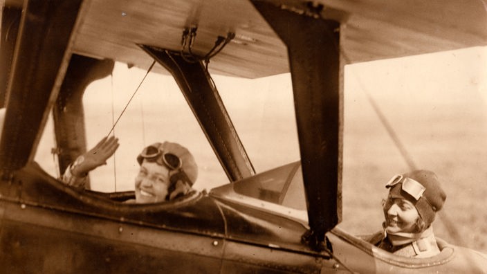 Zwei junge Frauen in einem offenen Doppeldecker-Flugzeug