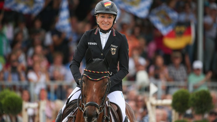 Eine Sportreiterin mit strahlendem Lächeln auf Pferd bei einem Wettbewerb