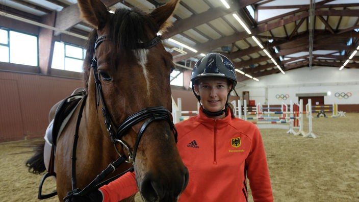Eine junge Frau steht neben einem Pferd und lächelt in die Kamera