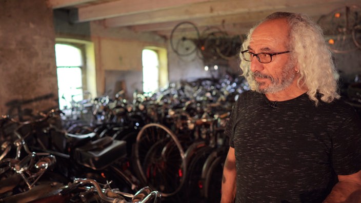 Ein Mann steht in einem Raum neben vielen historischen Fahrrädern 