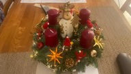Ein Adventskranz aus Tannenzwiegen mit roten Kerzen, goldenen Sternen und einer weihnachtlichen Dekofigur in der Mitte,
